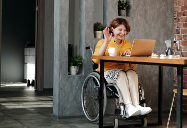 woman in wheelchair on laptop waving hello at the screen